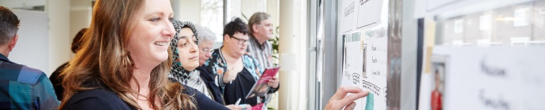 Groep mensen bekijkt flopovervellen die op een wand geplakt zijn 