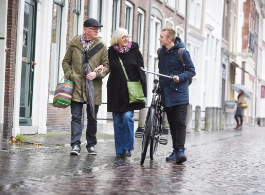 Twee ouderen en een jongen met fiets wandelen in de regen