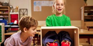 Decoratieve foto van twee kinderen die een Smaakles volgen op school. Een van de kinderen moet zonder te kijken raden wat ze in haar handen heeft. Dit zijn twee paprika's.